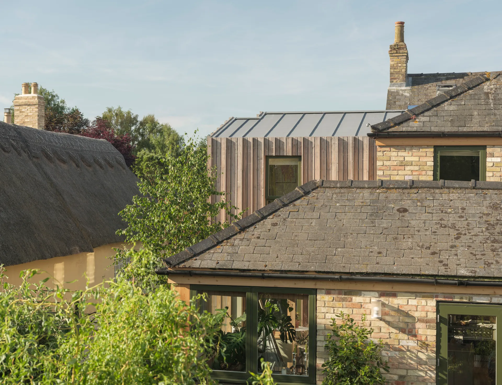 Butcher Bayley Architects Limited — East Croft, a playful timber addition with a standing-seam roof, set among neighbouring listed thatched cottages and tiled roofs