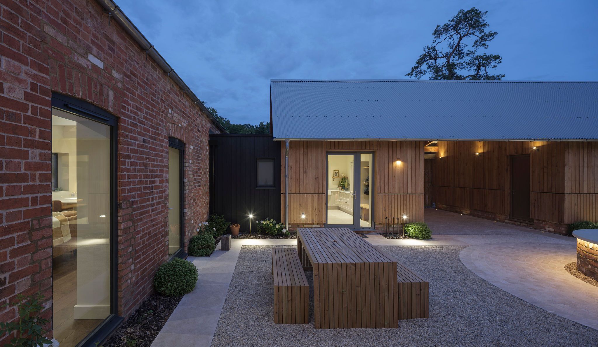 The Old Stables at dusk, showing a landscaped courtyard framed by restored brickwork and a timber-clad barn